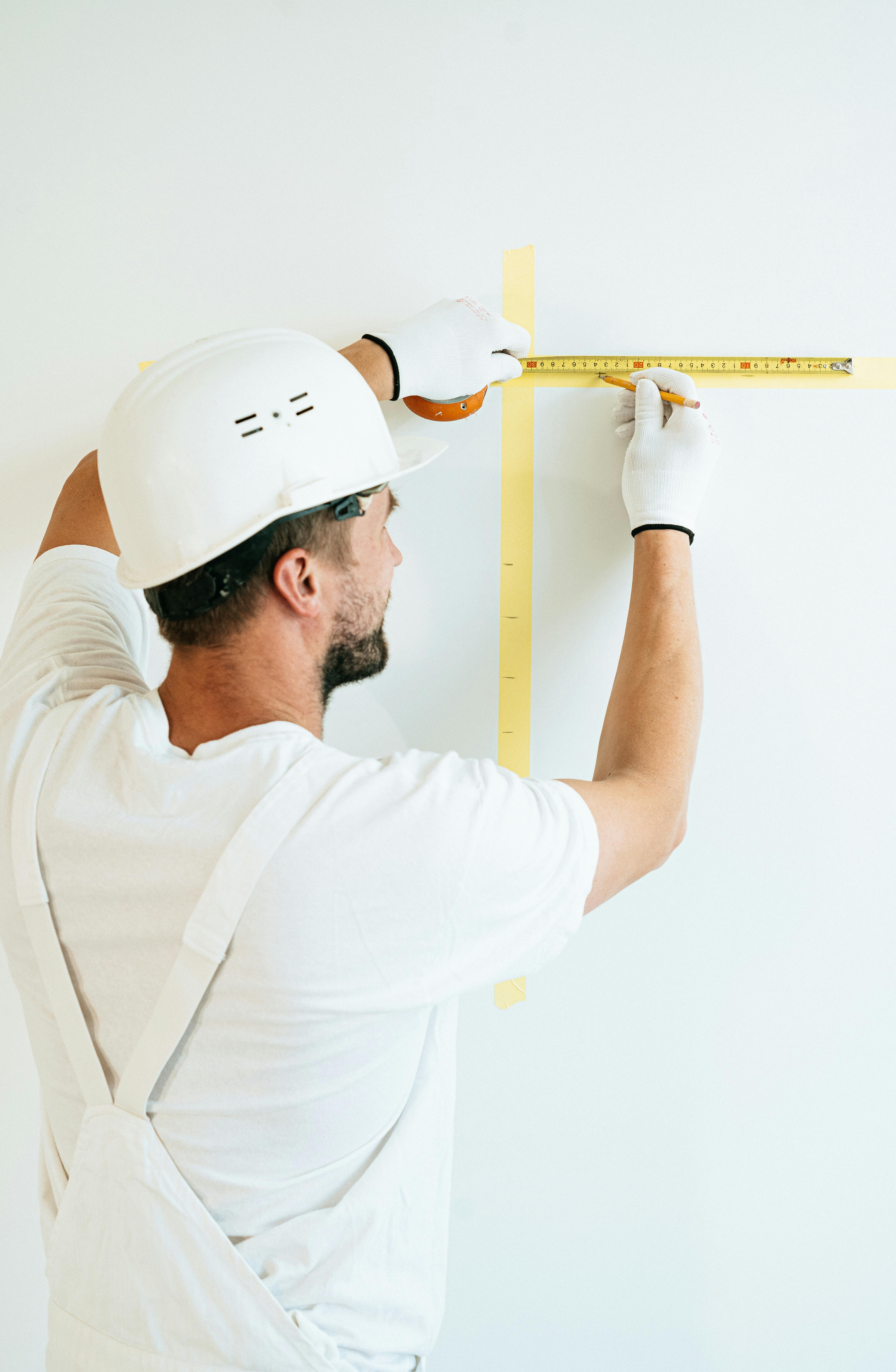 Artisan traçant au crayon un repère de hauteur sur un mur blanc, mètre ruban et bande adhésive